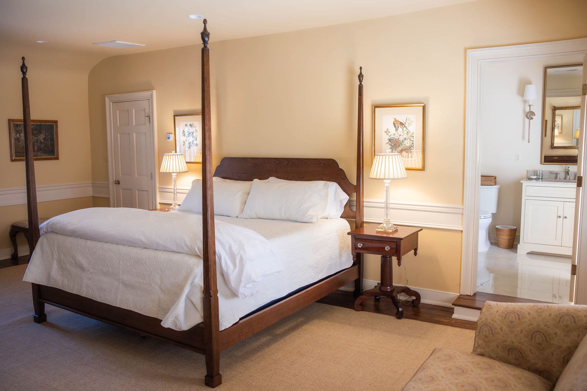 A cozy bedroom featuring a four-poster bed, bedside lamps, and an adjoining bathroom.