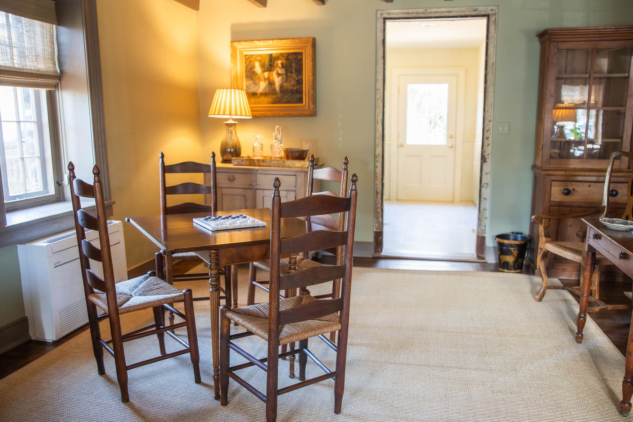A cozy dining area with a wooden table and chairs, featuring a lamp and an open doorway leading to another room.