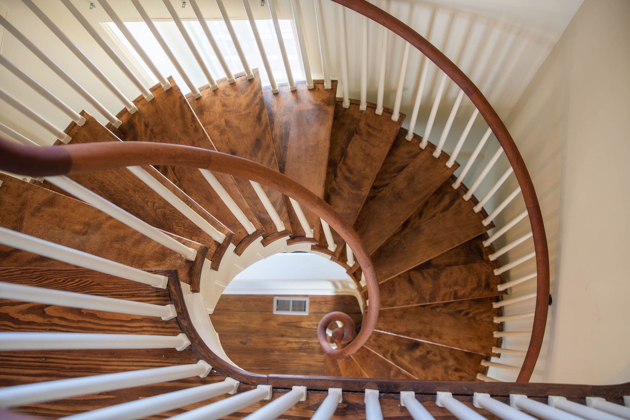 Spiral staircase viewed from above, featuring a wooden floor and white railings.