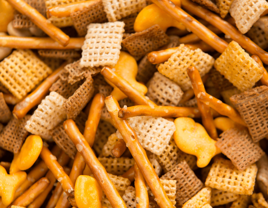 A close-up of a mix of snacks including cereal squares, pretzel sticks, and cheese crackers.