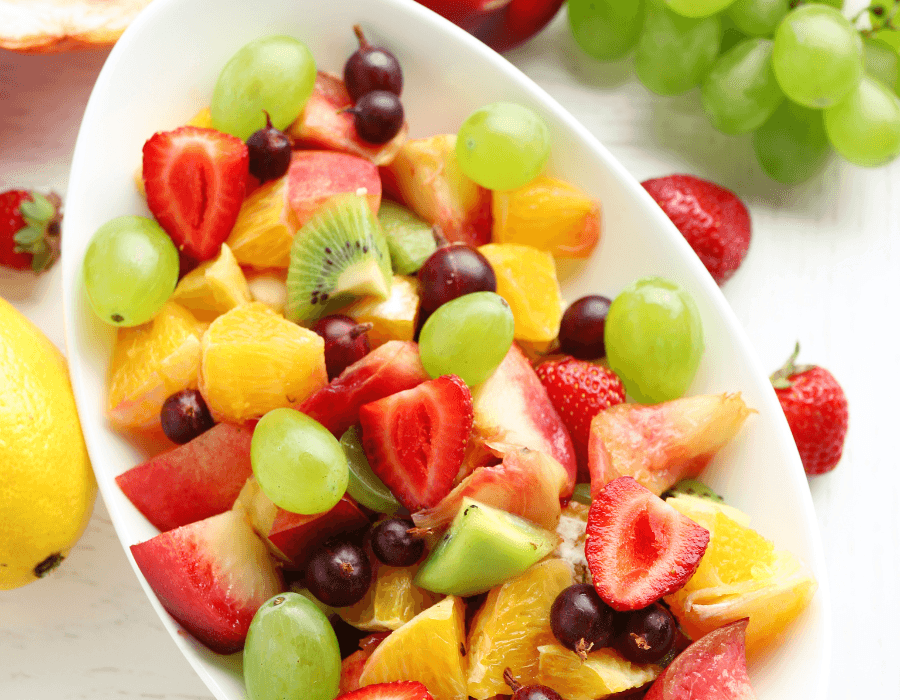 A colorful fruit salad featuring strawberries, grapes, kiwis, oranges, and apples in a white bowl.