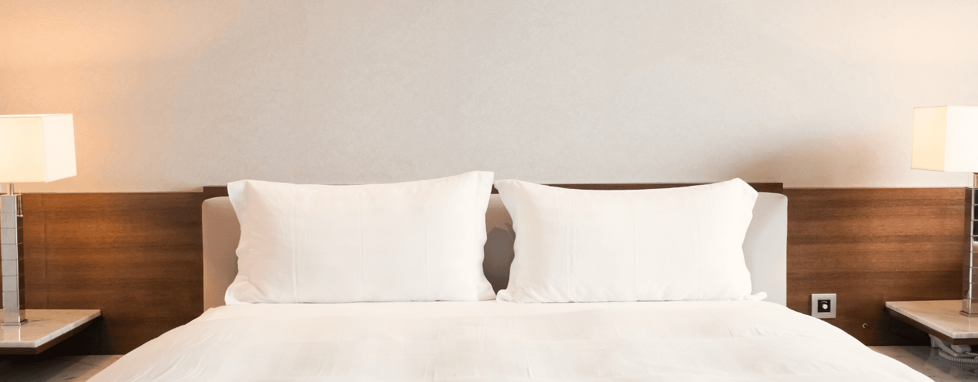 A neatly made bed with white pillows and soft lighting on either side.