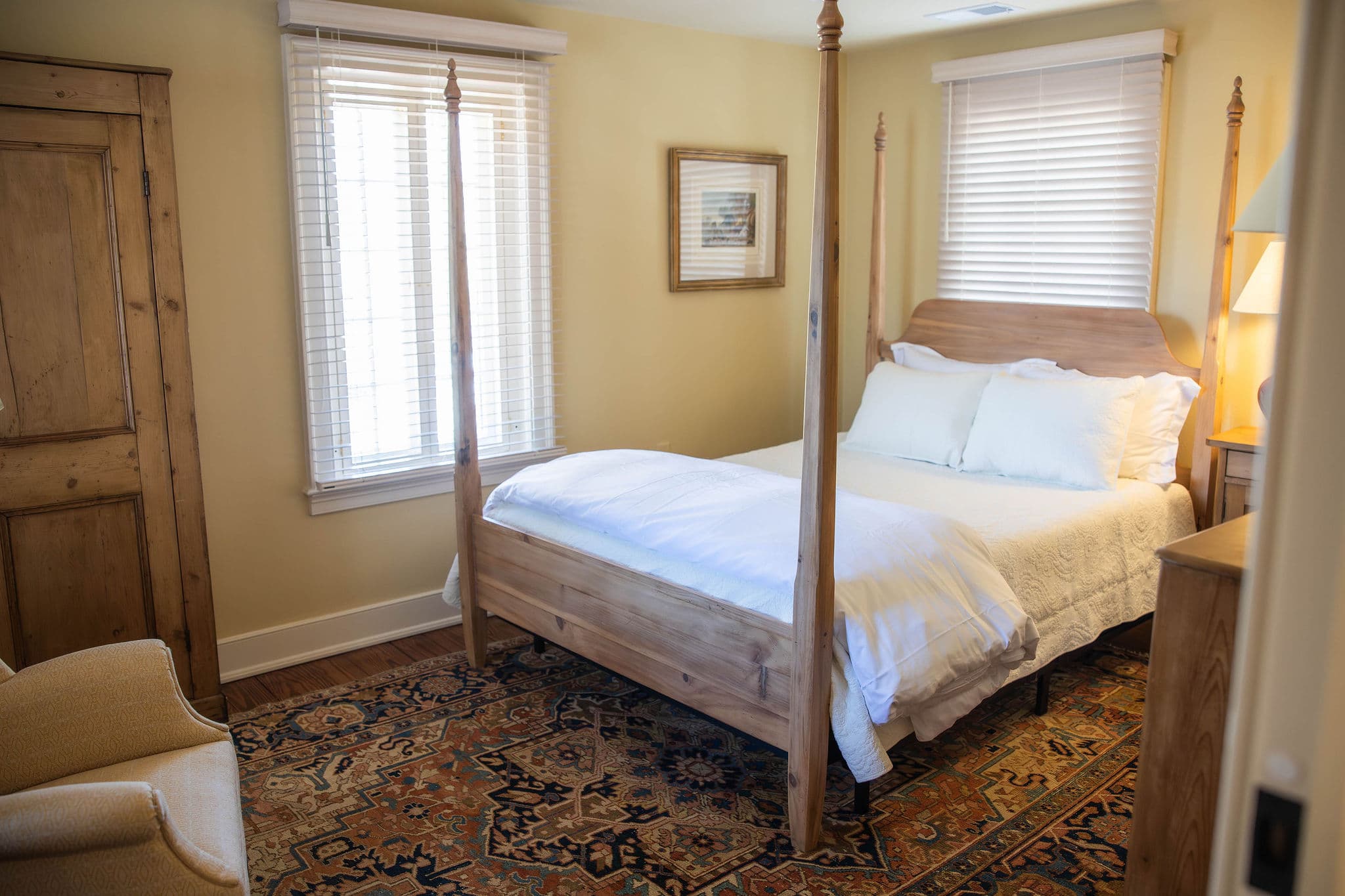 A cozy bedroom featuring a four-poster bed, light-colored walls, and a patterned rug.